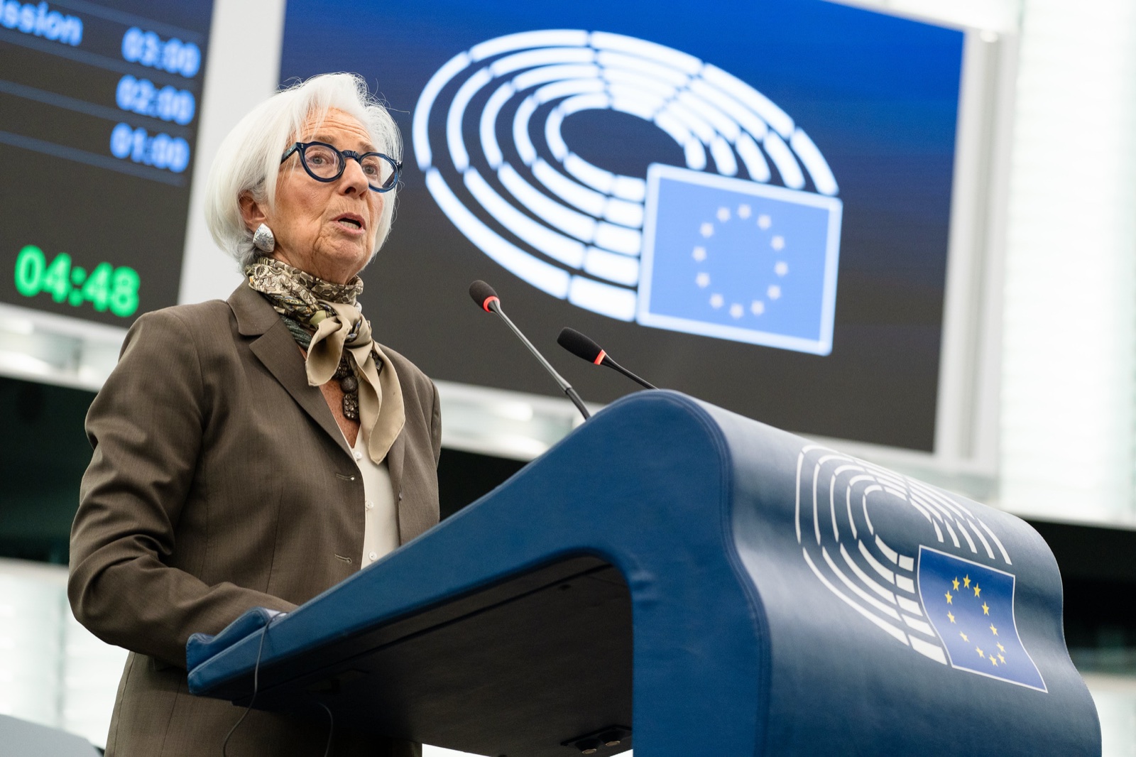 Christine Lagarde, de pelo blanco, gafas azules y pañuelo al cuello, habla en el atril del Parlamento Europeo.