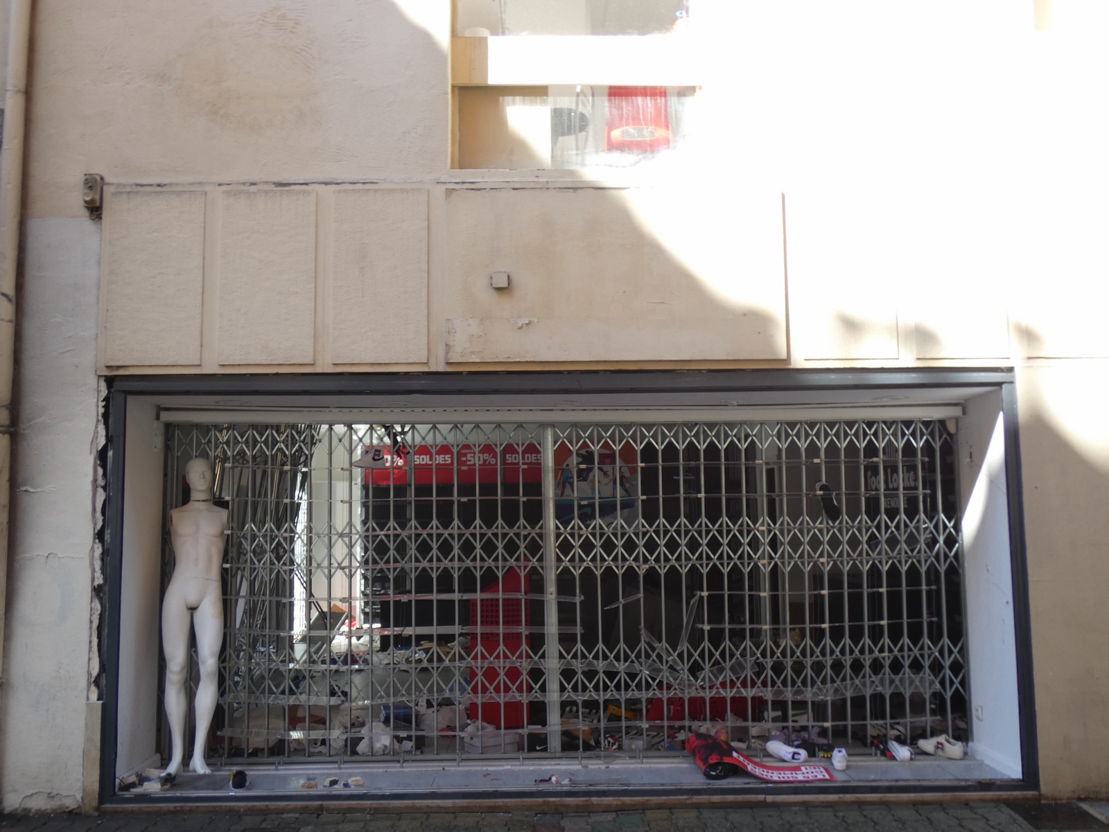Escaparate de una tienda de deporte sin cristal, con la reja metálica forzada, un maniquí y zapatillas tiradas por el suelo.