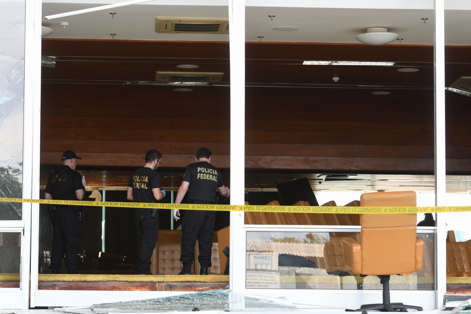 Tres agentes con camisetas de la Policía Federal inspeccionan una sala de butacas tras unas cristaleras rotas y una cinta policial amarilla.
