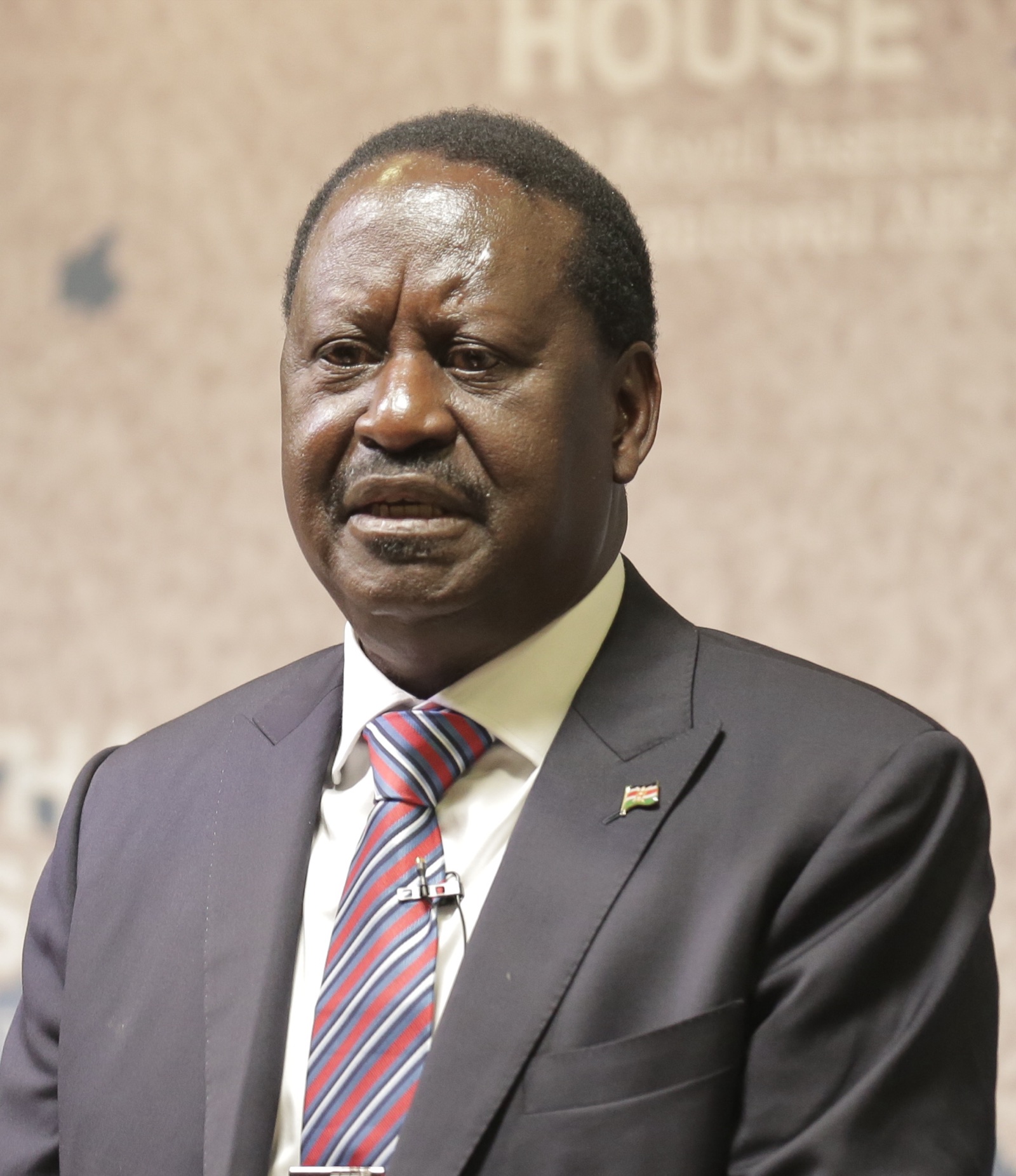 Raila Odinga, con traje oscuro y corbata de rayas, habla con un micrófono de solapa ante un fondo con el rótulo de Chatham House.