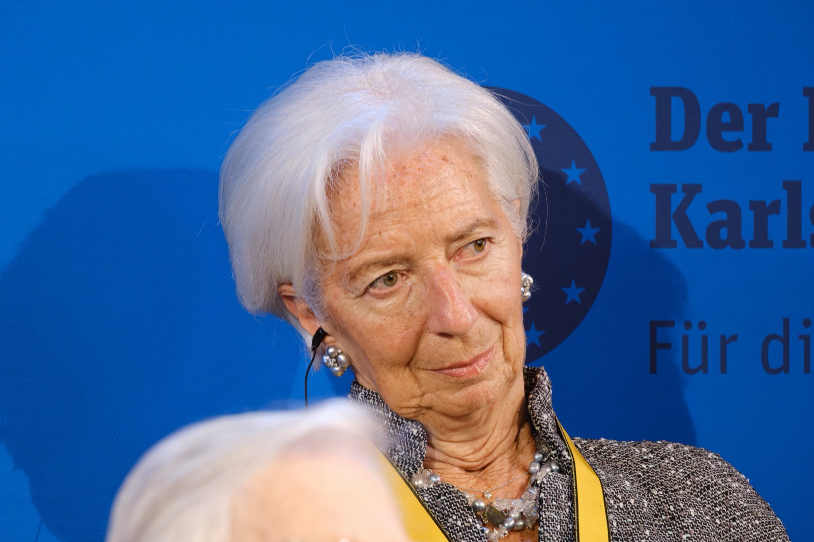 Christine Lagarde, de pelo blanco y pendientes de perlas, mira a un lado ante un fondo azul con estrellas.