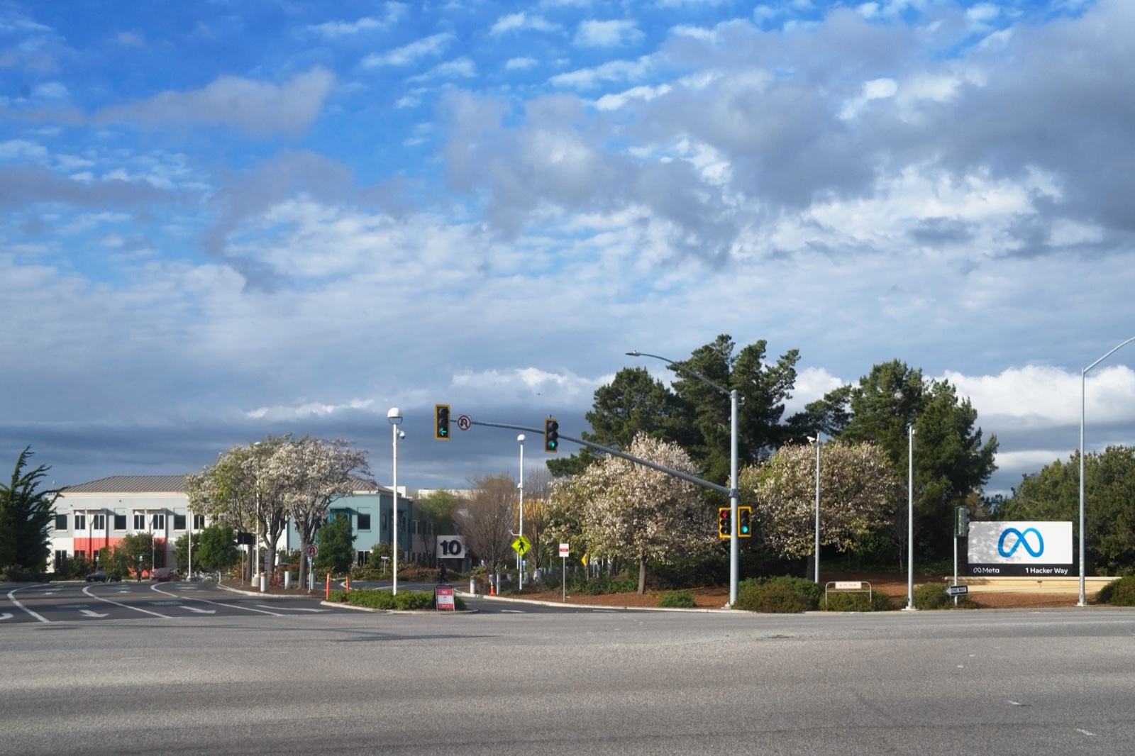 Cruce de carreteras con semáforos ante la sede de Meta: árboles en flor, edificios bajos al fondo y, a la derecha, un cartel blanco con el logotipo azul de Meta.